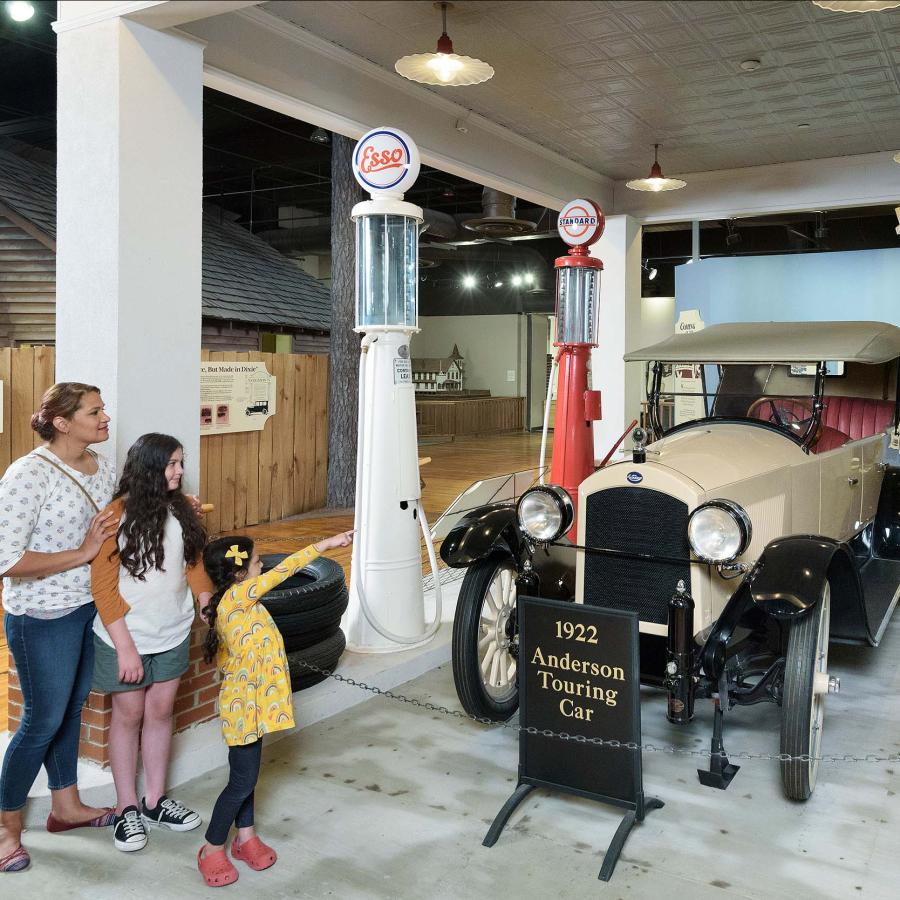 Mom and 2 daughters stand look at a white, early 20th century vintage car on display at the SC State Museum