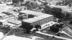 Arial views shows large 'L' shaped brick building with canal alongside it