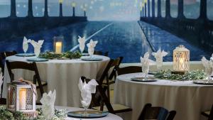 Three formally set table with the white table cloths and napkins with painted mural of bridge in the background