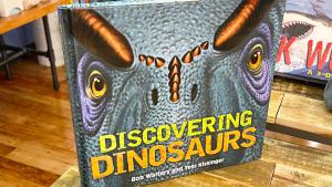 Book With Close Up Dinosaur face on the cover with a title in yellow that read Discovering Dinosaurs