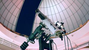 Large white telescope points towards the dark night sky under a partially open observatory 