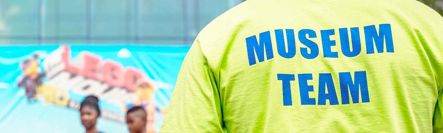Man faces away from camera in neon yellow shirt with "Museum Team" written across the back in blue letters