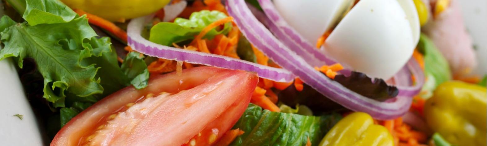 Close up of salad with lettuce, peppers, red onion, boiled egg and shredded carrot