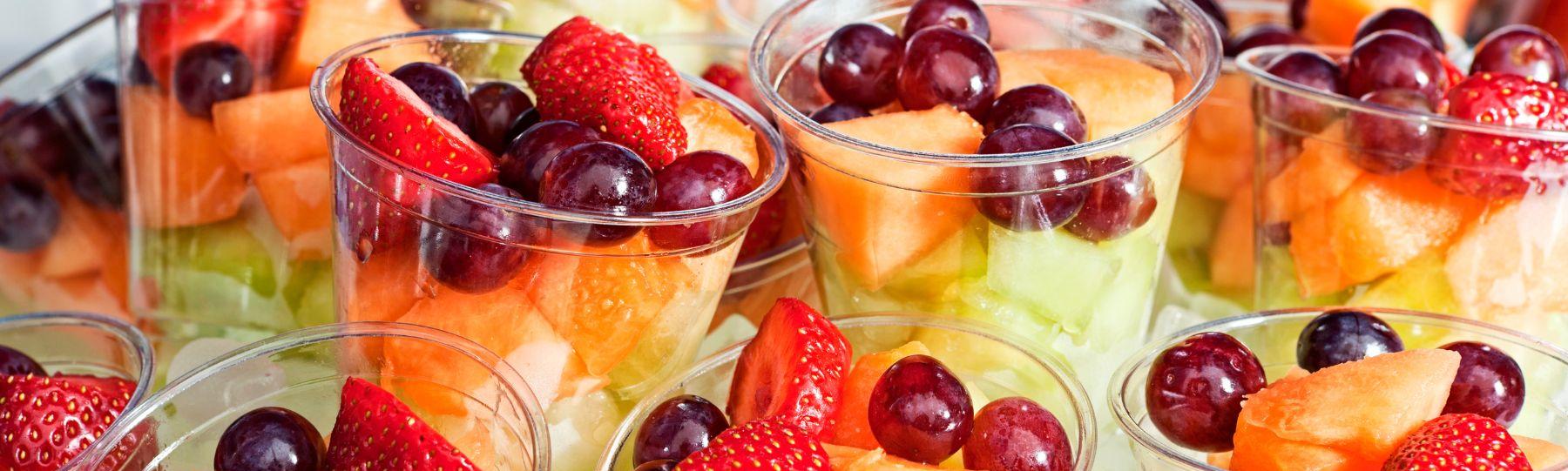 Small plastic cups filled with cut up fruit including grapes and strawberries