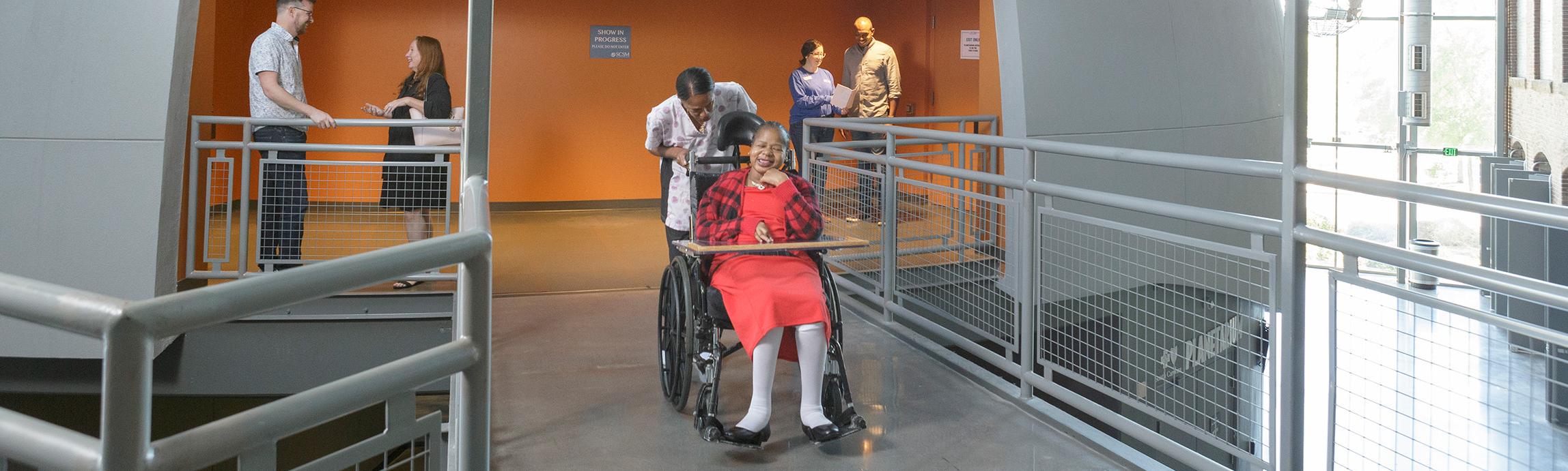 Large dome structure with exit midway up onto a catwalk space. Guest in wheelchair is on catwalk with caretaker and other guests in the background.