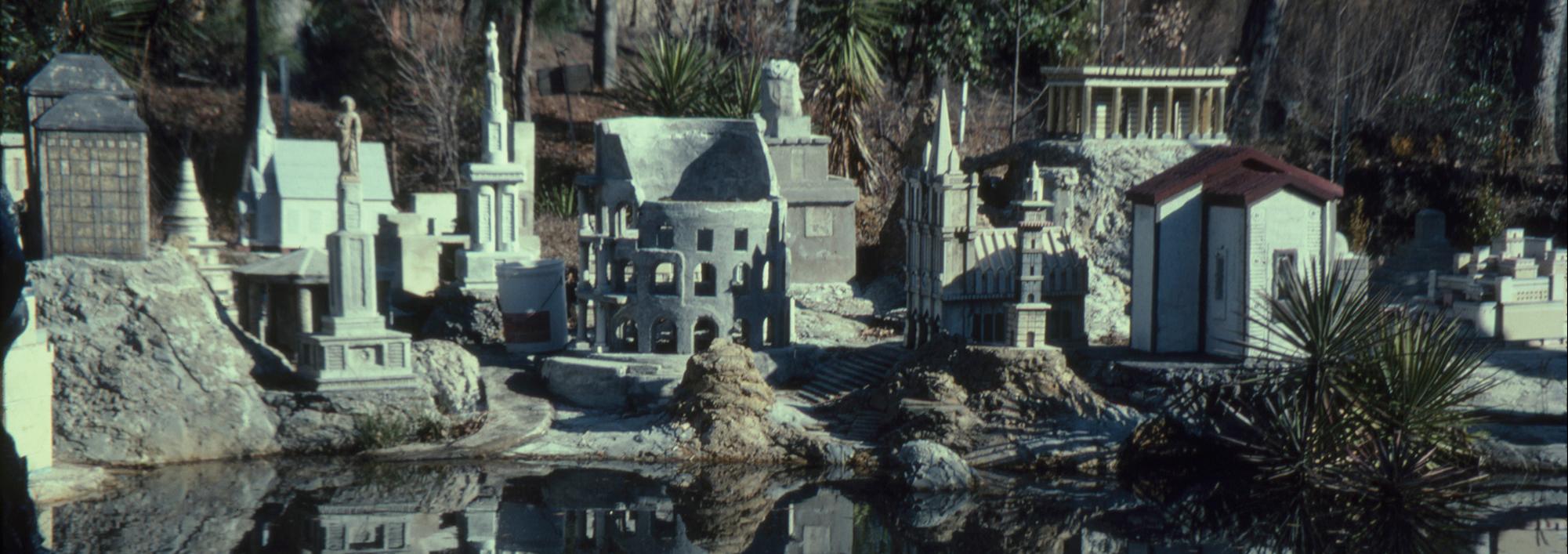 Collection of large building replicas of classical architecture made in concrete set up outdoors with a small pond in the foreground