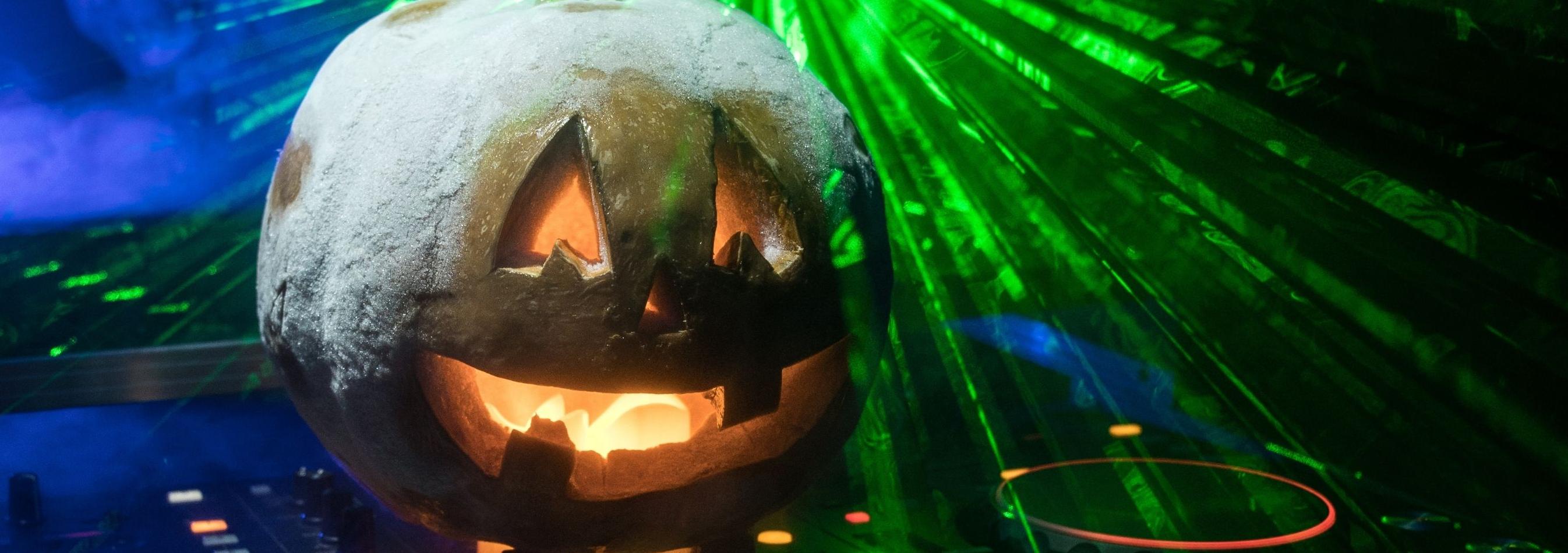 Jack O lantern sitting on DJ turntables with green lasers behind it