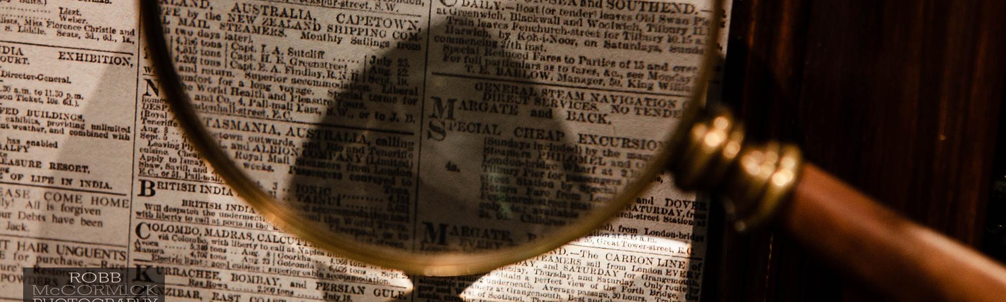 Close up image of magnifying glass with brass rim and a newspaper in the background