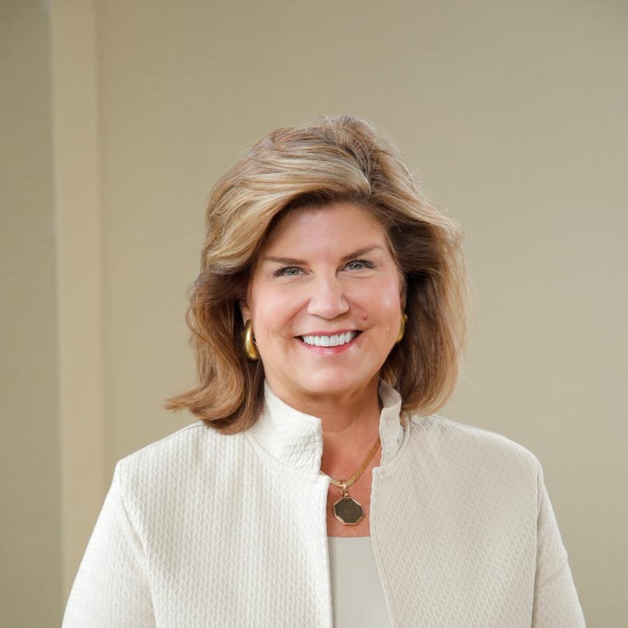 Women with shoulder length hair and a cream suit jacket smiles