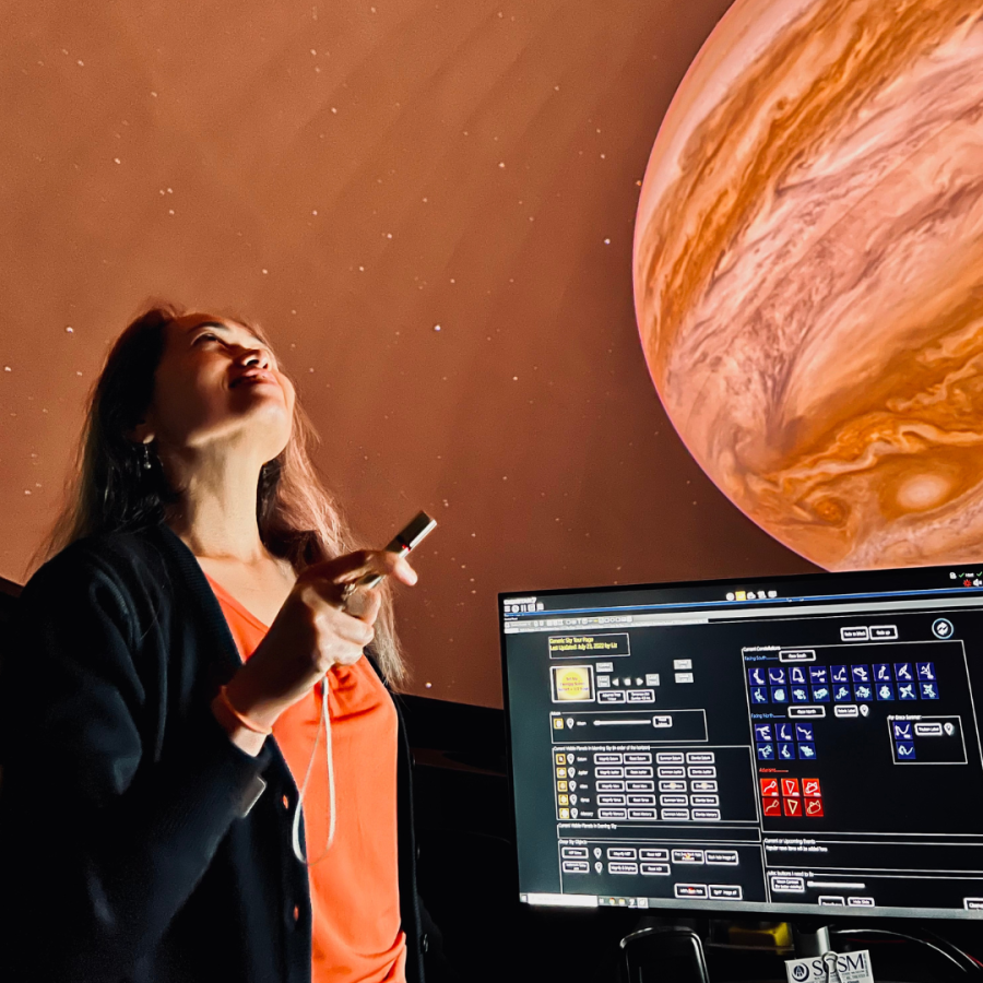 Woman looks up projection of Jupiter on planetarium dome while holding small flashlight