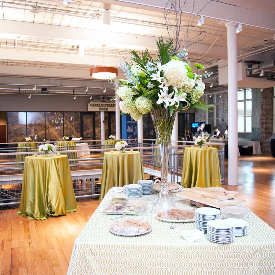 Table with white tablecloth and white dishes with Large white floral arrangement set up in an open space with wood flooring