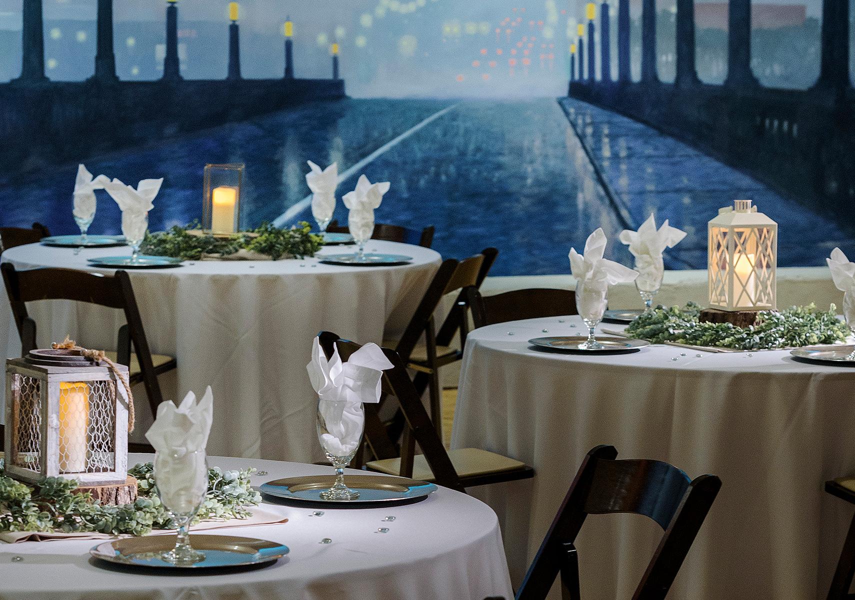Three formally set table with the white table cloths and napkins with painted mural of bridge in the background