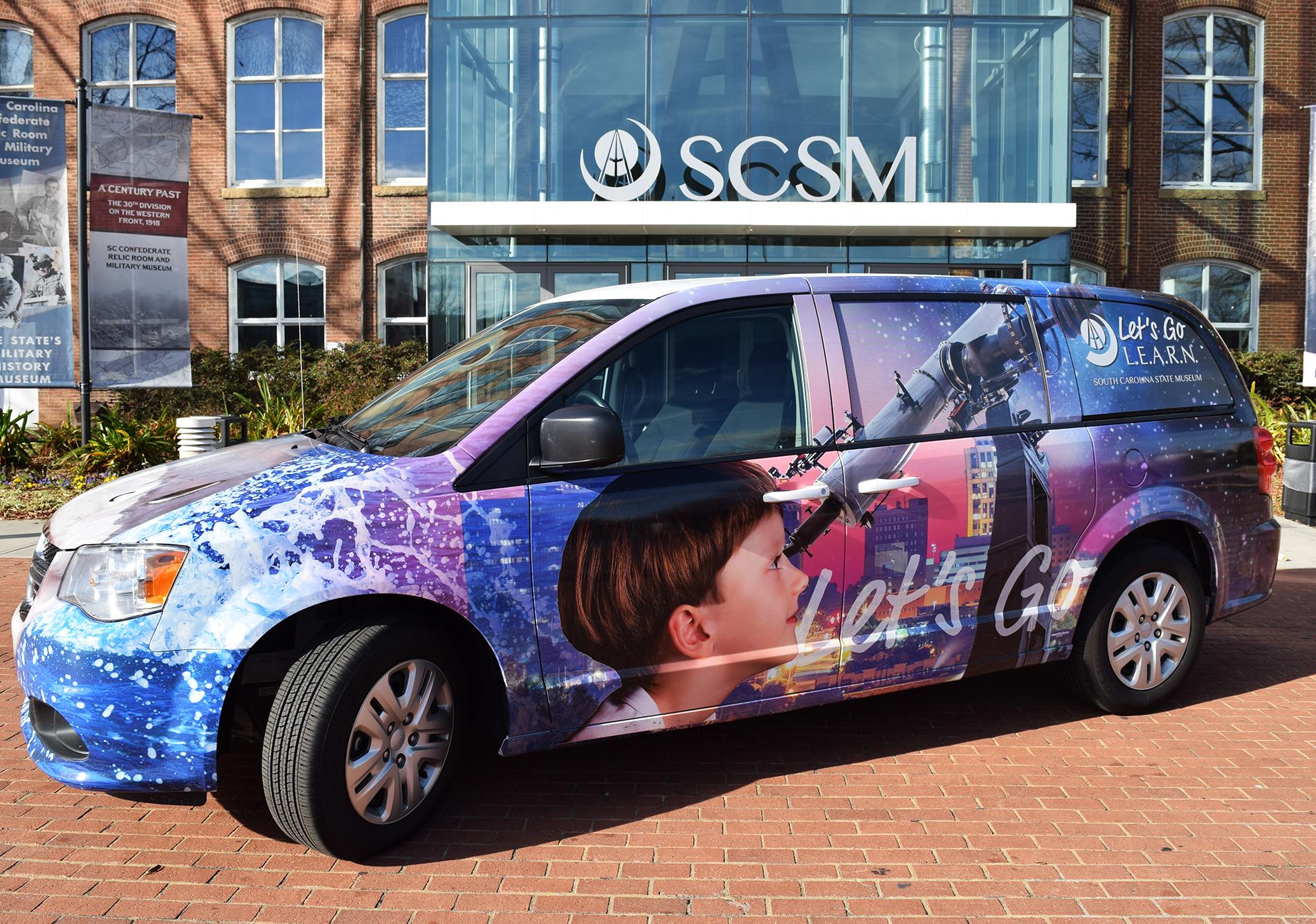 Van decorated with artwork that shows a boy looking through a telescope is parked in front of the museum's main entrance