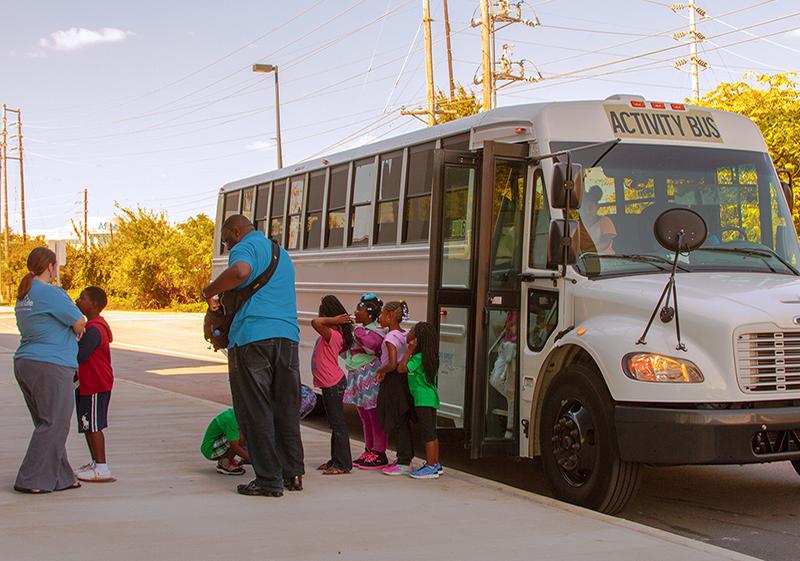 Group of small students and two adults exits a white bus parked next to the South Carolina State Museum