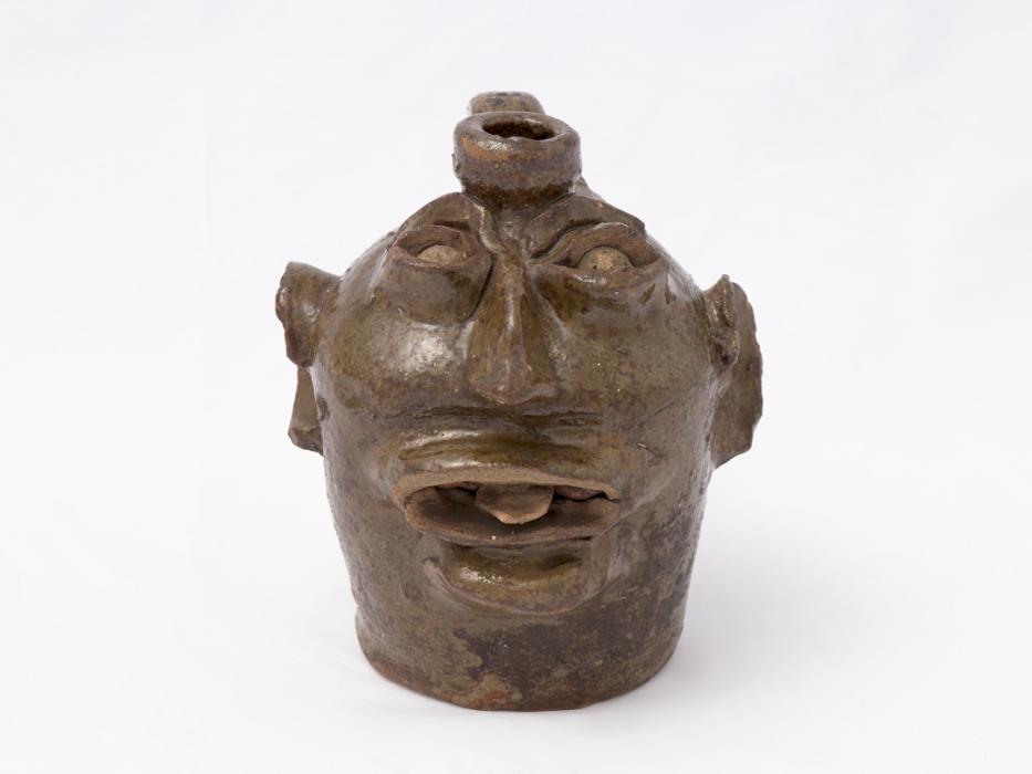 Small ceramic jug with image of face fashioned into its side with its tongue sticking out