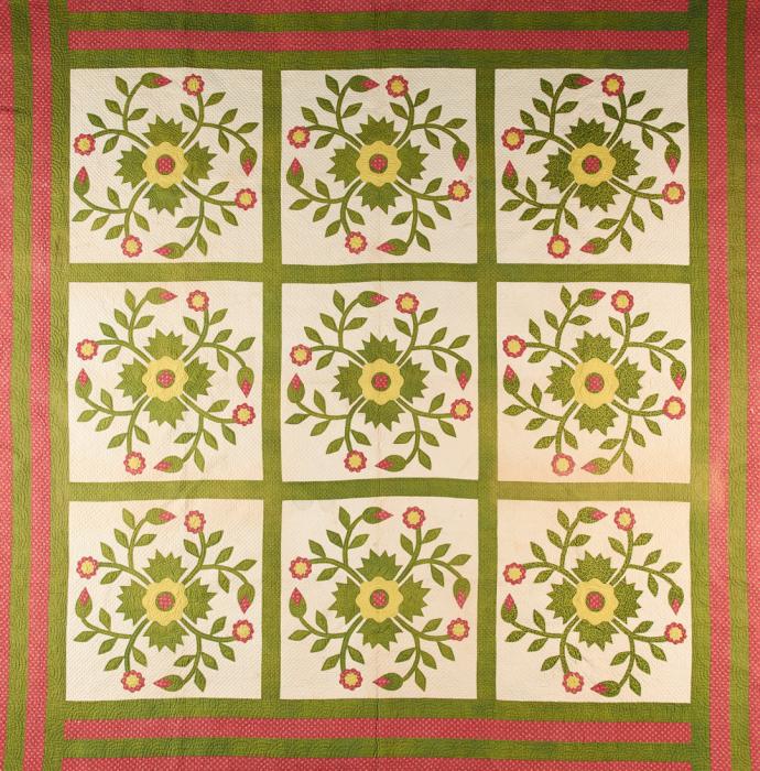 Quilt with red and green border and cream center divided into 6 squares each featuring the same vine and flower design in green red and yellow.