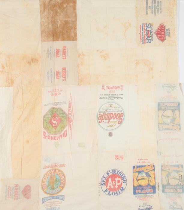 Quilt made in large squares of feed sacks with brand names like "Self-Rising AP Flour" visible.